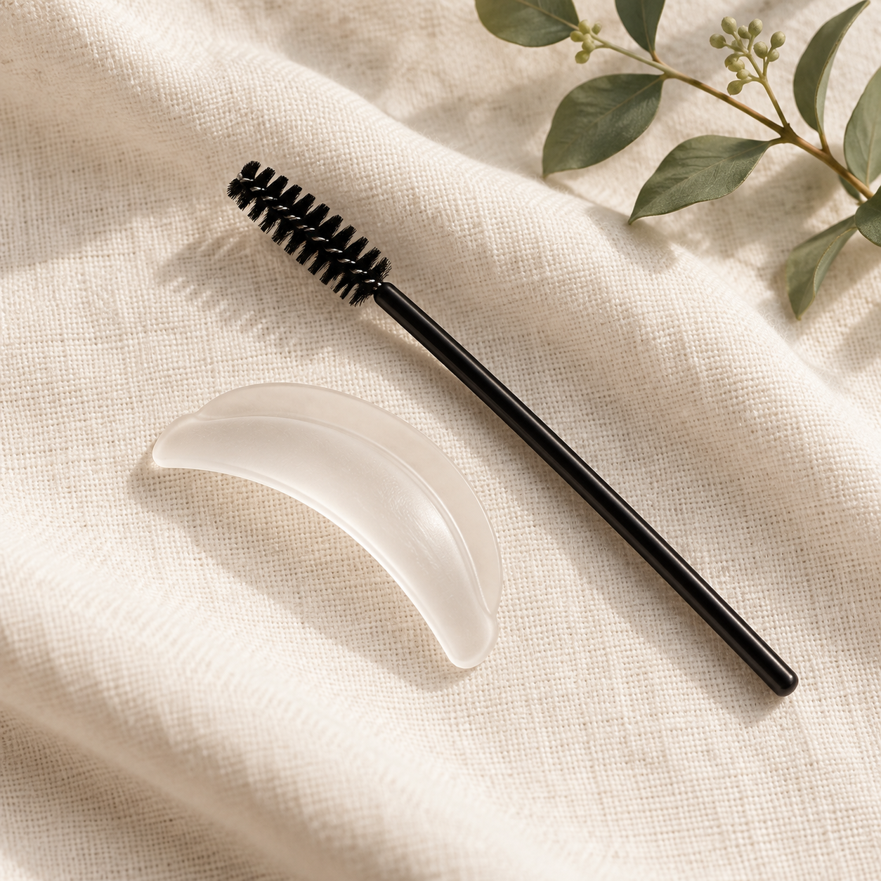 Lash lift shield and spoolie arranged on ivory linen
